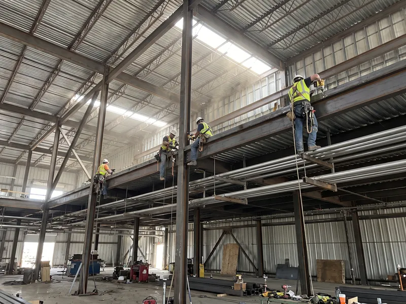 Ironworkers bolting a structural steel mezzanine inside a manufacturing building