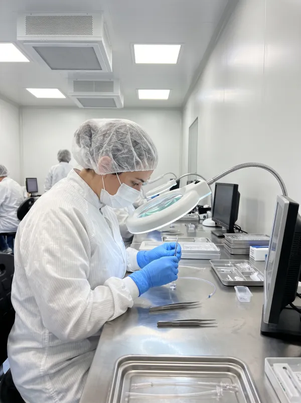 Cleanroom technician assembling a catheter component under a magnifier