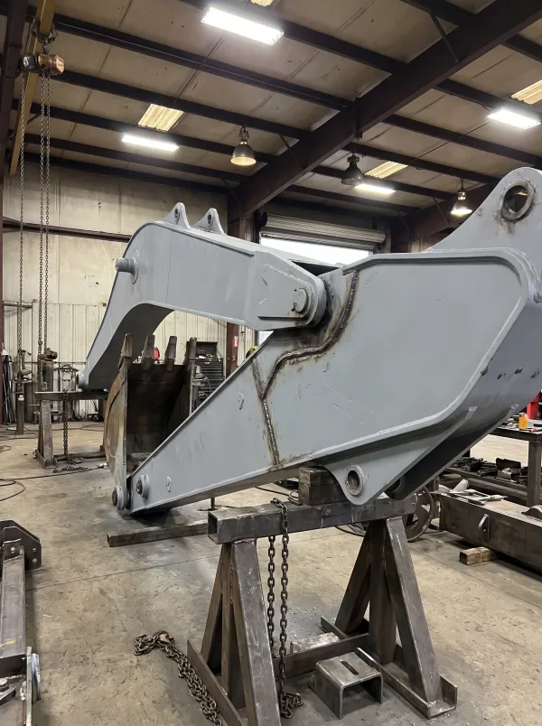 Fabricated excavator boom arm on stands in a fabrication bay