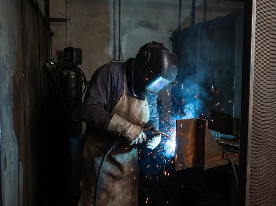Welder in an auto-darkening helmet MIG welding a heavy steel bracket